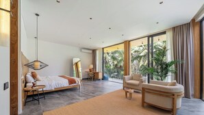 Ein modernes Schlafzimmer mit Bett, Sofa, Schreibtisch und einem großen Fenster mit Blick auf Palmen.