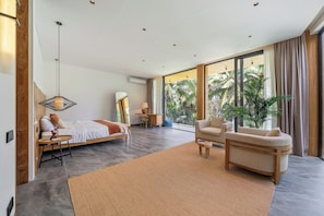Ein modernes Schlafzimmer mit Bett, Sofa, Schreibtisch und einem großen Fenster mit Blick auf Palmen.