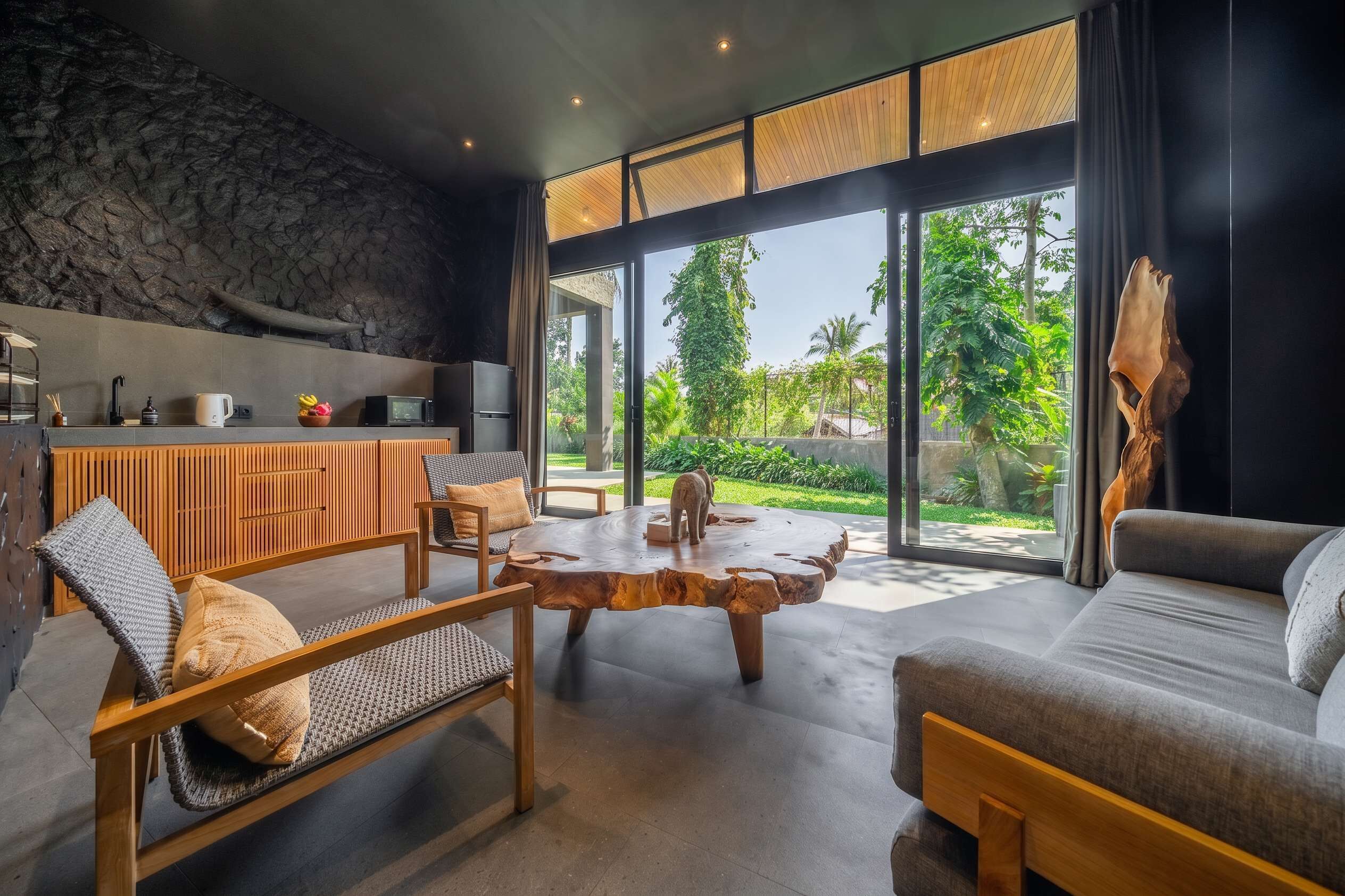 A modern living room with a stone wall, a wooden dining area, and a large glass door leading to a garden.