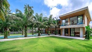 Ein modernes, zweistöckiges Haus mit Swimmingpool, umgeben von üppiger Vegetation und Palmen.
