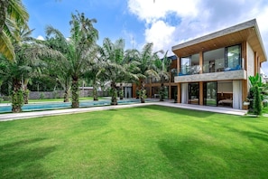 Ein modernes, zweistöckiges Haus mit Swimmingpool, umgeben von üppiger Vegetation und Palmen.