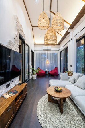 A modern living room with a large flat-screen TV, a wooden coffee table, a white sofa, and red bean bags. - Luxe 2BR Villa in Ubud w Garden Bath, Patio & Pool (Gianyar Regency)