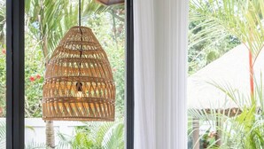 Una habitación con un ventanal grande, una lámpara colgante de mimbre, un sillón de bola rojo y una mesita con un libro y un objeto decorativo.