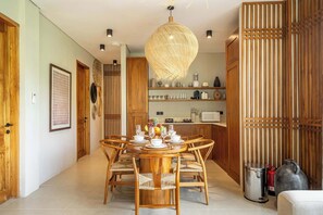 A dining area with a round wooden table, wicker chairs, and a hanging light fixture. - Cozy 3BR Villa in Lush Ubud w Pool, Patio & Garden (Gianyar Regency)