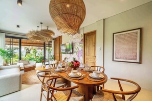 A modern dining area with a wooden table set for four, surrounded by wicker chairs. - Cozy 3BR Villa in Lush Ubud w Pool, Patio & Garden (Gianyar Regency)