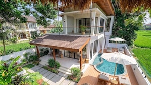 A two-story house with a swimming pool, outdoor seating, and lush greenery. - Cozy 3BR Villa in Lush Ubud w Pool, Patio & Garden (Gianyar Regency)