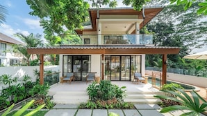 A modern two-story house with a covered patio, outdoor seating, and lush greenery. - Cozy 3BR Villa in Lush Ubud w Pool, Patio & Garden (Gianyar Regency)