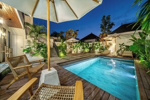 Ein Schwimmbecken mit Liegestühlen und Sonnenschirmen, umgeben von Pflanzen und einer Holzterrasse.