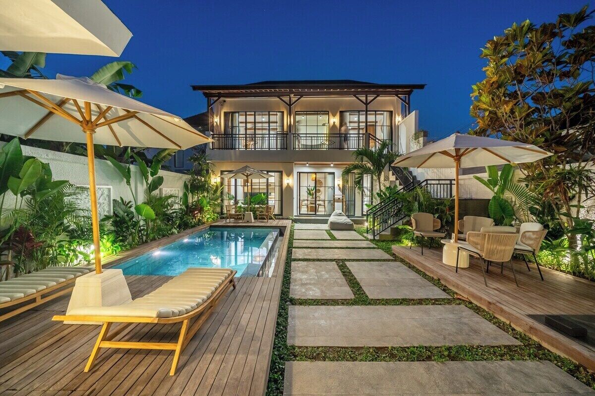 A two-story house with a swimming pool, outdoor furniture, and tropical plants.