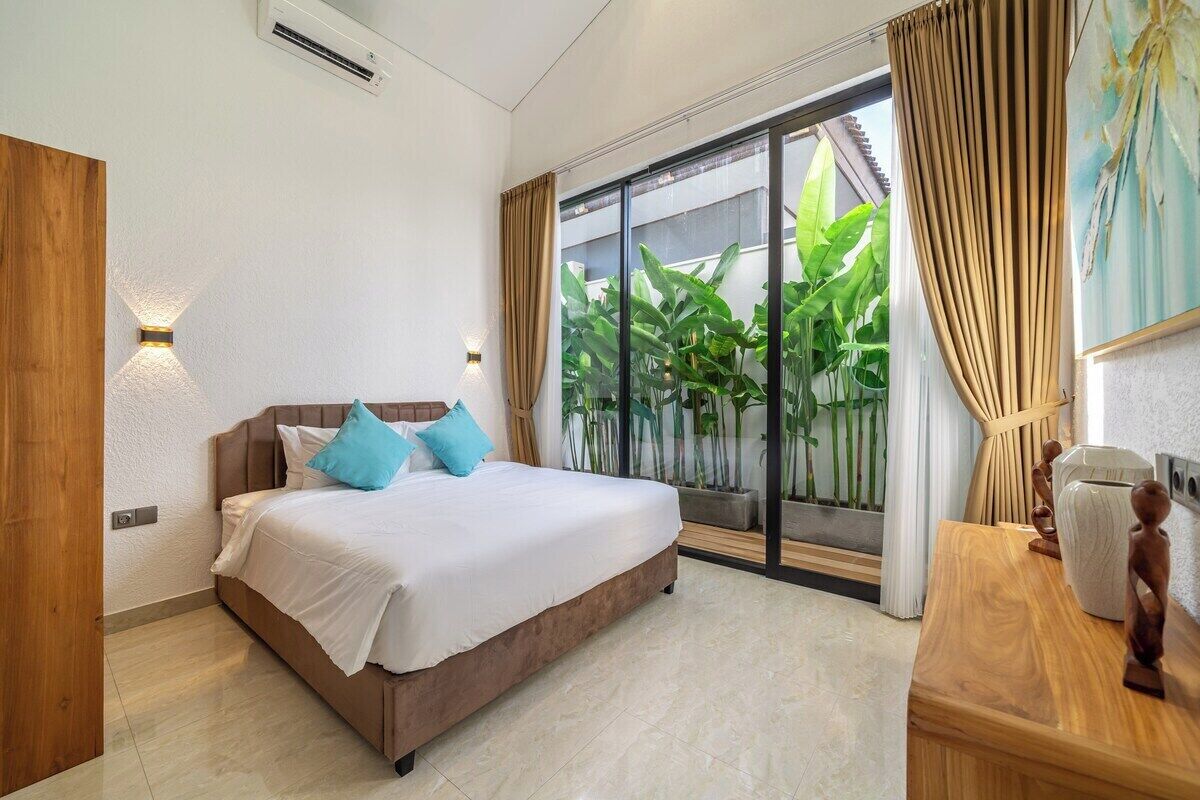 Une chambre à coucher avec un lit, des lampes de chevet, une table de chevet en bois et une vue sur la verdure grâce à une porte-fenêtre coulissante.