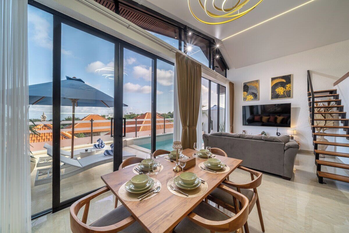Un espace de repas moderne avec une grande table dressée pour quatre personnes, un canapé et un téléviseur dans un salon.