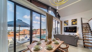 Un comedor moderno con una mesa grande dispuesta para cuatro personas, un sofá y un televisor en una sala de estar.
