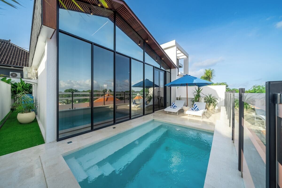 Un espace piscine extérieur moderne, doté de parois en verre, de chaises longues et de parasols.
