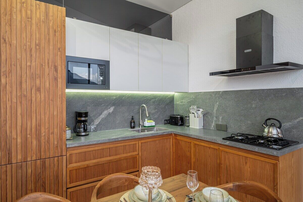 Une cuisine moderne avec des meubles en bois, un four à micro-ondes encastré, une cuisinière à gaz et une bouilloire en acier inoxydable.