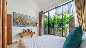 Un dormitorio con una cama grande, un cuadro en la pared, una ventana con plantas y una mesita de noche de madera.