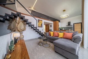 Una sala de estar moderna con un sofá gris, una mesa de centro de madera y una escalera con barandillas negras.