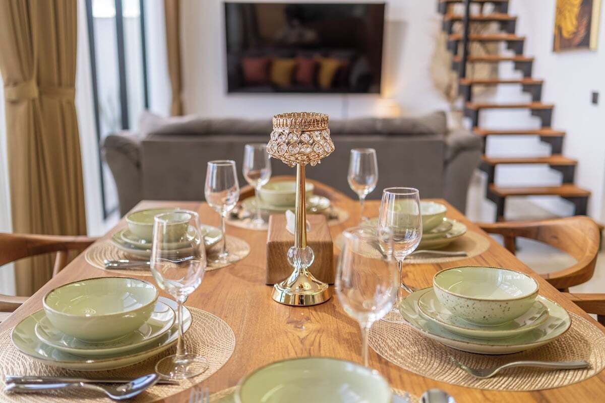 Une table à manger dressée avec de l’assiette verte, des verres transparents et une lampe décorative.