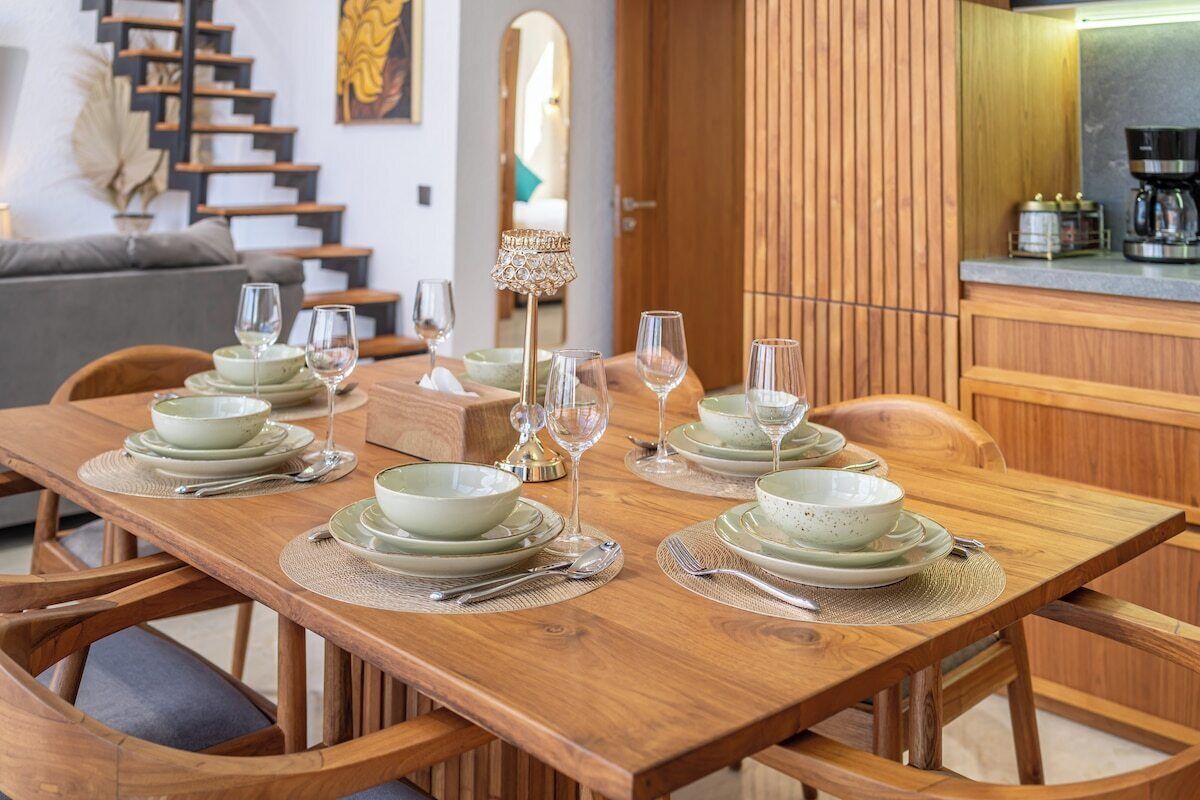 Un coin repas avec une table en bois, dressée pour quatre personnes, entourée de chaises.