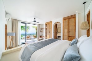 A modern hotel room with a large bed, a ceiling fan, a view of the outdoors, and a balcony with outdoor furniture. - Luxe 4BR Villa w Rooftop, Cinema, Ocean View (Badung Regency)