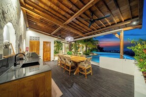 A modern kitchen with a wooden ceiling, a dining area with a pool view, and a poolside setting. - Luxe 4BR Villa w Rooftop, Cinema, Ocean View (Badung Regency)