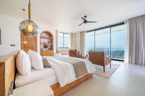 A modern bedroom with a large bed, a ceiling fan, and a view of the city. - Luxe 4BR Villa w Rooftop, Cinema, Ocean View (Badung Regency)