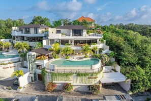 A modern multi-story hotel with a pool, surrounded by lush greenery. - Luxe 4BR Villa w Rooftop, Cinema, Ocean View (Badung Regency)