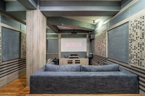 A modern interior with a grey sofa, a projector screen displaying 'NETFLIX,' and a wooden cabinet with audio equipment. - Luxe 4BR Villa w Rooftop, Cinema, Ocean View (Badung Regency)