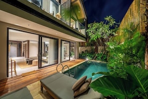 A modern house with a swimming pool, glass doors leading to a living area, and lush greenery. - Badung's 2BR Gem w Private Pool & Beach Nearby (Badung Regency)