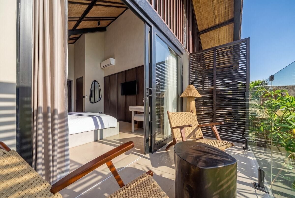 Un dormitorio moderno con cama, televisor y puerta corrediza de vidrio que da a un balcón con una silla y una mesa.