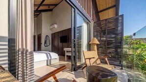 A modern bedroom with a bed, a TV, and a sliding glass door leading to a balcony with a chair and a table. - Badung's 2BR Gem w Private Pool & Beach Nearby (Badung Regency)
