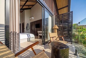 A modern bedroom with a bed, a TV, and a sliding glass door leading to a balcony with a chair and a table. - Badung's 2BR Gem w Private Pool & Beach Nearby (Badung Regency)