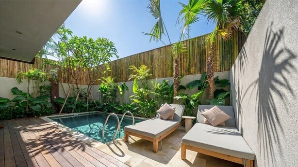 A poolside area with wooden decking, lounge chairs, and a bamboo wall. - Badung's 2BR Gem w Private Pool & Beach Nearby (Badung Regency)