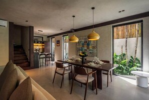 A modern dining area with a wooden table, chairs, and pendant lighting. - Badung's 2BR Gem w Private Pool & Beach Nearby (Badung Regency)
