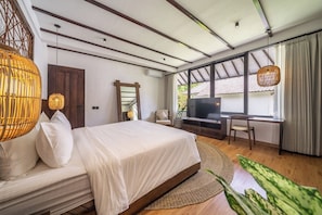 Ein Schlafzimmer mit Bett, Schreibtisch, Fernseher und großen Fenstern.