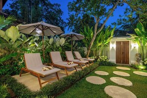 A garden with lounge chairs and umbrellas, a wooden door, and a stone pathway. - Tropical 3BR Villa in Ubud w Pool, Patio & Garden (Ubud)