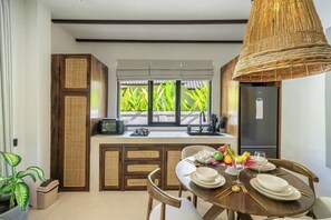Eine moderne Küche mit Essbereich, ausgestattet mit einem großen Fenster mit Blick auf Grünflächen, einem eingebauten Kühlschrank und einer Pendelleuchte.