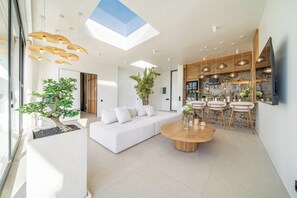A modern living space with a white sofa, a round wooden coffee table, and a dining area with chairs. - Brand New Chic 2BR Villa, Beach Access, South Kuta (South Kuta)