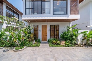 Ein modernes, zweistöckiges Haus mit Holztür, kleiner Veranda und gepflasterter Auffahrt.