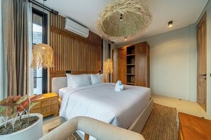 A modern hotel room with a large bed, a bedside table, a chair, a potted plant, and a unique woven ceiling light fixture. - Tropical 2BR in Ubud's Ricefields w Pool & Garden (Tegallalang)