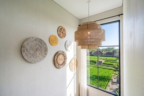 A room with a large window, a hanging light fixture, and several wall-mounted decorative plates. - Serene 2BR Retreat w Spacious Pool & Garden • Ubud (Gianyar Regency)