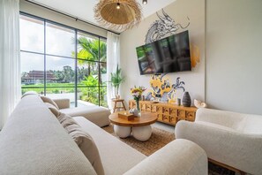 A modern living room with a large window, a flat-screen TV, a sofa set, a wooden coffee table, and decorative items. - Tranquil 2BR Villa in Ubud • Pool • Patio • Garden (Gianyar Regency)