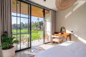 A bedroom with a bed, a desk, and a chair, a large window with a view of a green landscape, and a potted plant. - Tranquil 2BR Villa in Ubud • Pool • Patio • Garden (Gianyar Regency)