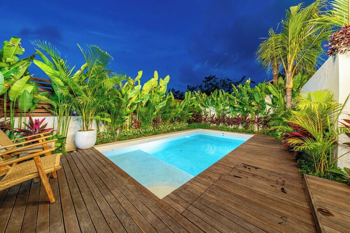 A wooden deck with a swimming pool, surrounded by lush tropical plants.