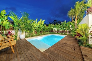 A wooden deck with a swimming pool, surrounded by lush tropical plants.