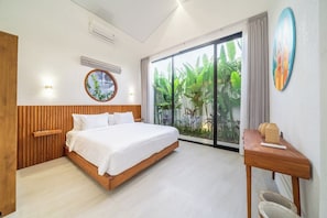 A bedroom with a bed, a wooden headboard, a bedside table, a wall-mounted air conditioner, a window with a view of greenery, and a circular wall decoration.
