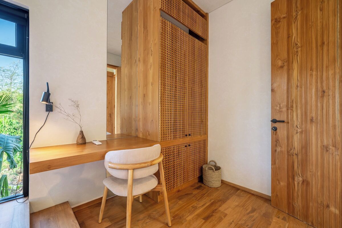 A room with a wooden desk, a chair, a woven partition, a door, and a small basket on the floor.