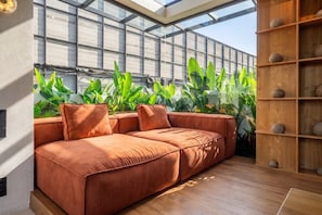 Ein modernes Interieur mit einem Ecksofa, einem Holzregal und einem großen Fenster mit Blick auf Grünflächen.