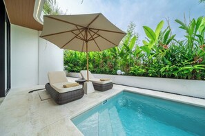 Ein Poolbereich mit Liegestühlen, Sonnenschirm und üppiger Bepflanzung.