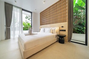 A modern bedroom with a large bed, a bedside table, and a view of greenery through a window. - Modern 2BR in Ungasan's Best w Beach Access+Pool (Badung Regency)