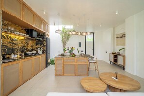 A modern kitchen with a central island, wooden cabinetry, and a dining area with a round table. - Modern 2BR in Ungasan's Best w Beach Access+Pool (Badung Regency)